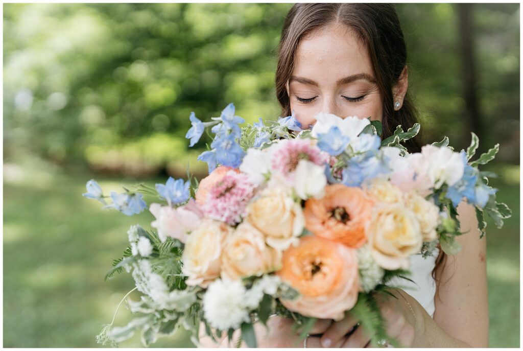 the bride smiles as she sniffs her wedding bouquet full of orange, pink and blue flowers 