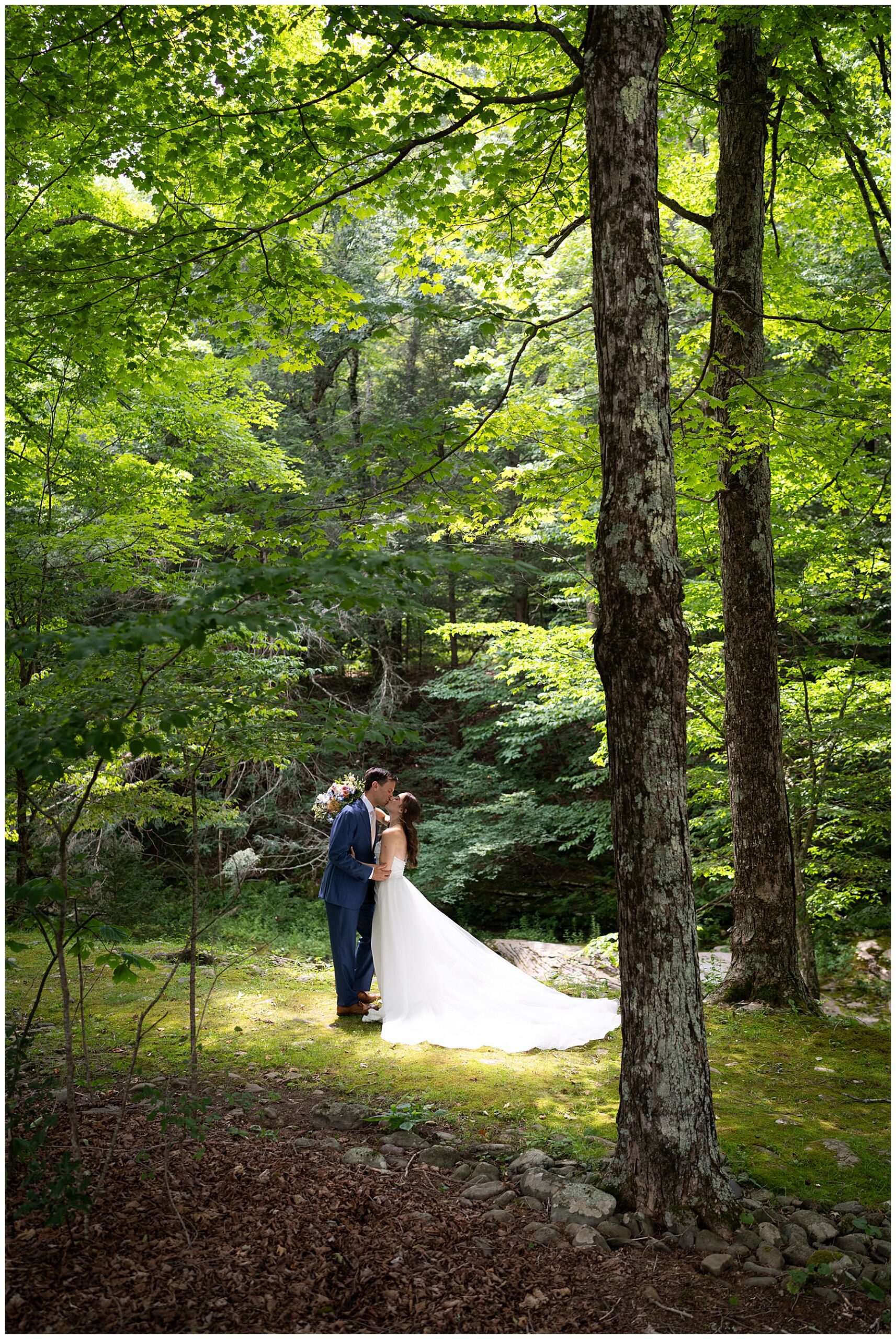 the bride and groom kissing as they stand in a sun spot within the forest of the catskills 