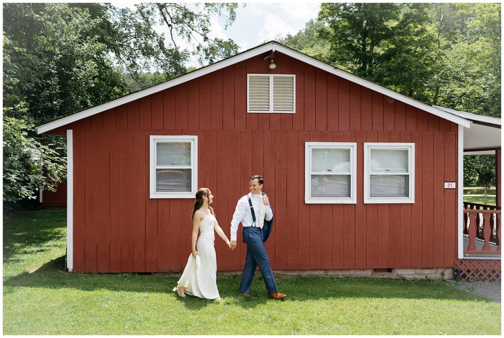 the bride and groom walking in front of a red cottage smiling at each other at their Full Moon Resort wedding