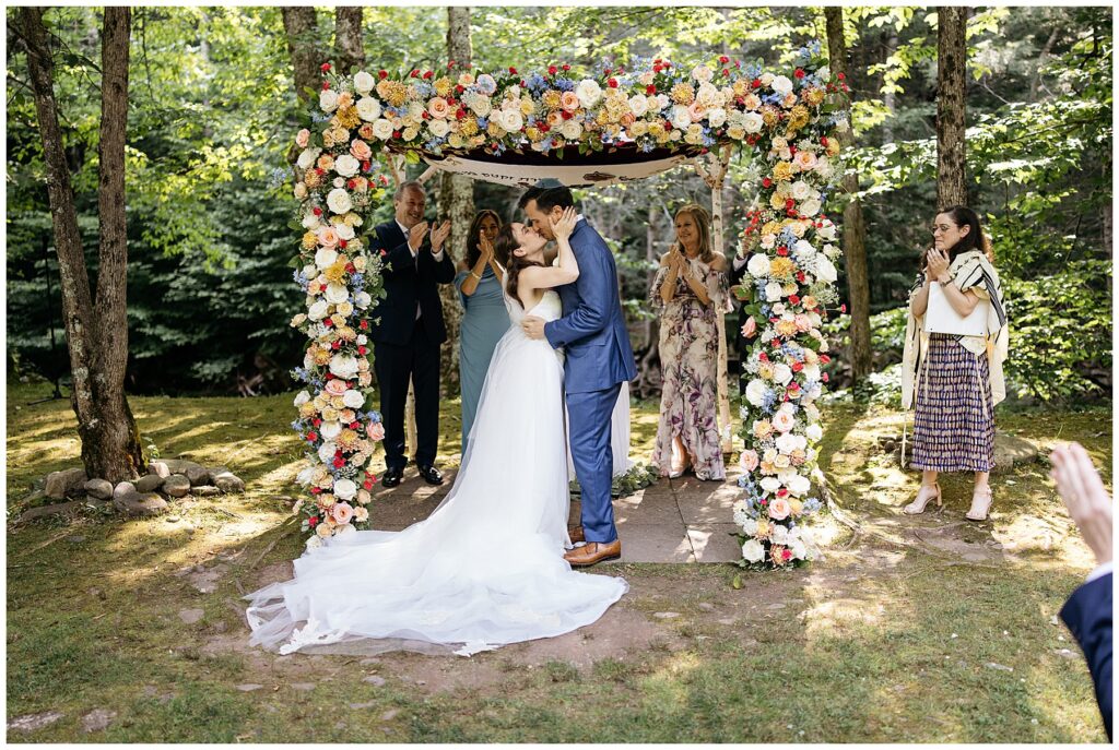 the bride and groom kissing under the flower-covered chuppah at the end of the wedding ceremony at full moon resort 