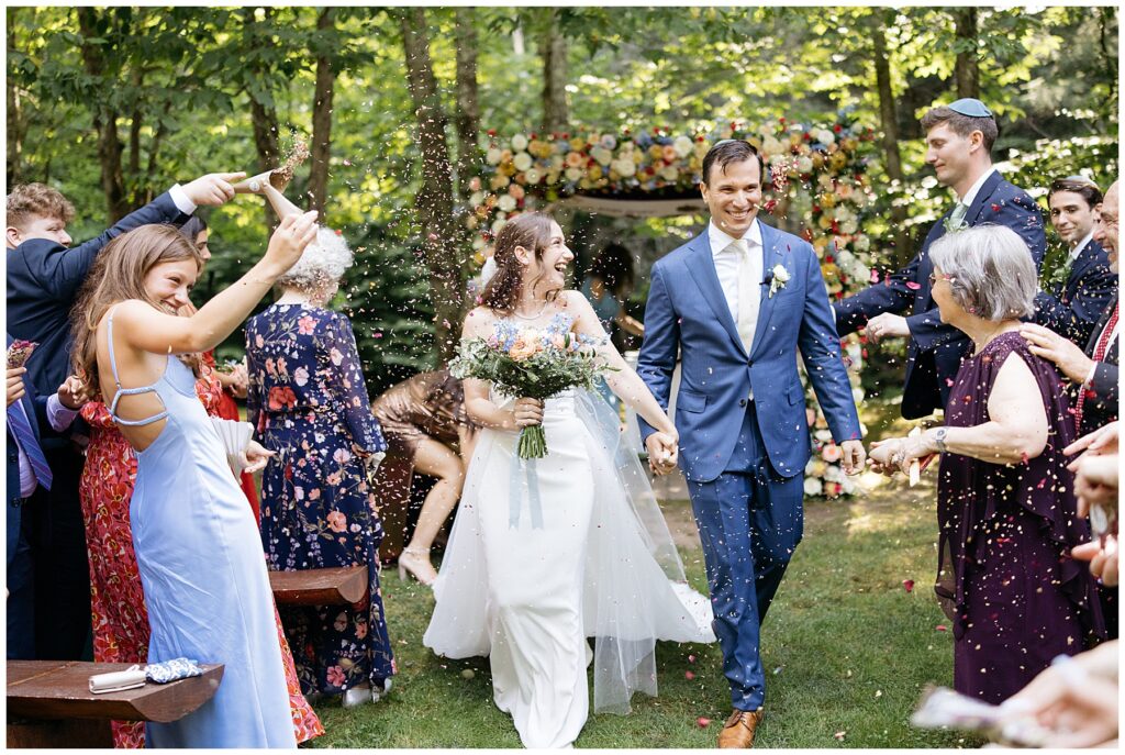 the bride and groom walking down the aisle smiling after the ceremony as the guests throw brightly colored confetti into the air around them 