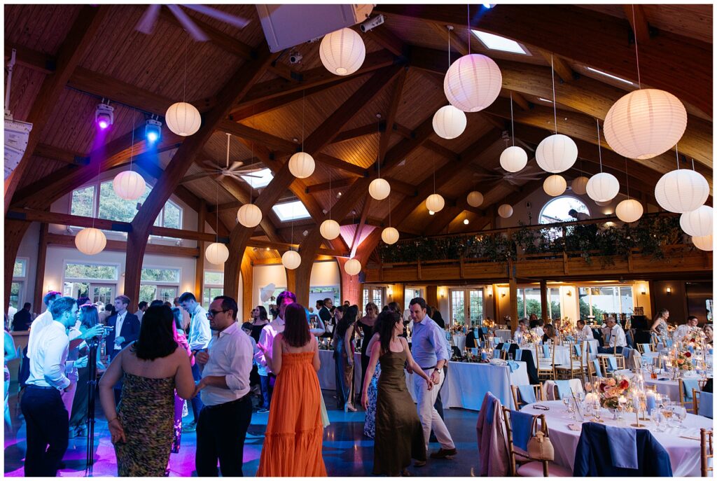 a wide shot of the reception space at full moon resort with an arched wood ceiling, circular lantern lights, and the guests dancing in the center 