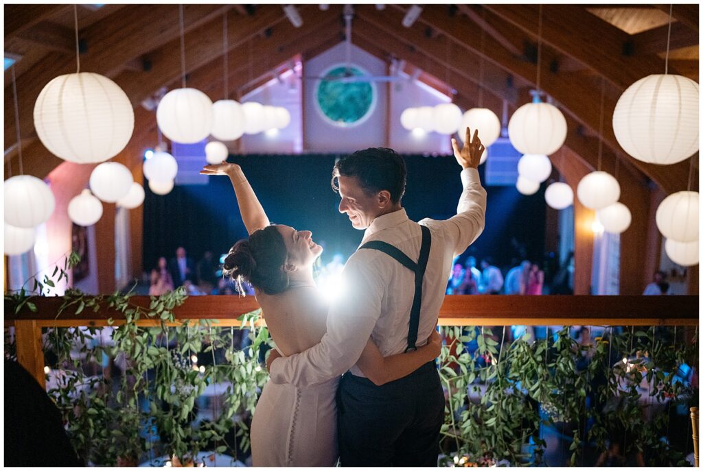 the bride and groom standing in the balcony of the reception space overlooking the wedding party below at full moon resort 